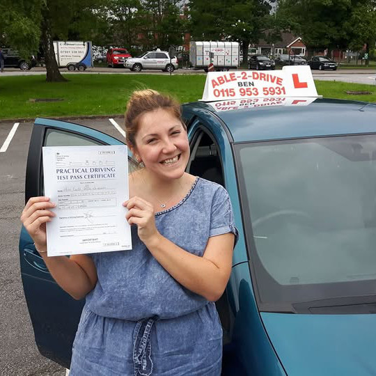 A person holding a driving test pass certificate in front of an Able 2 Drive car